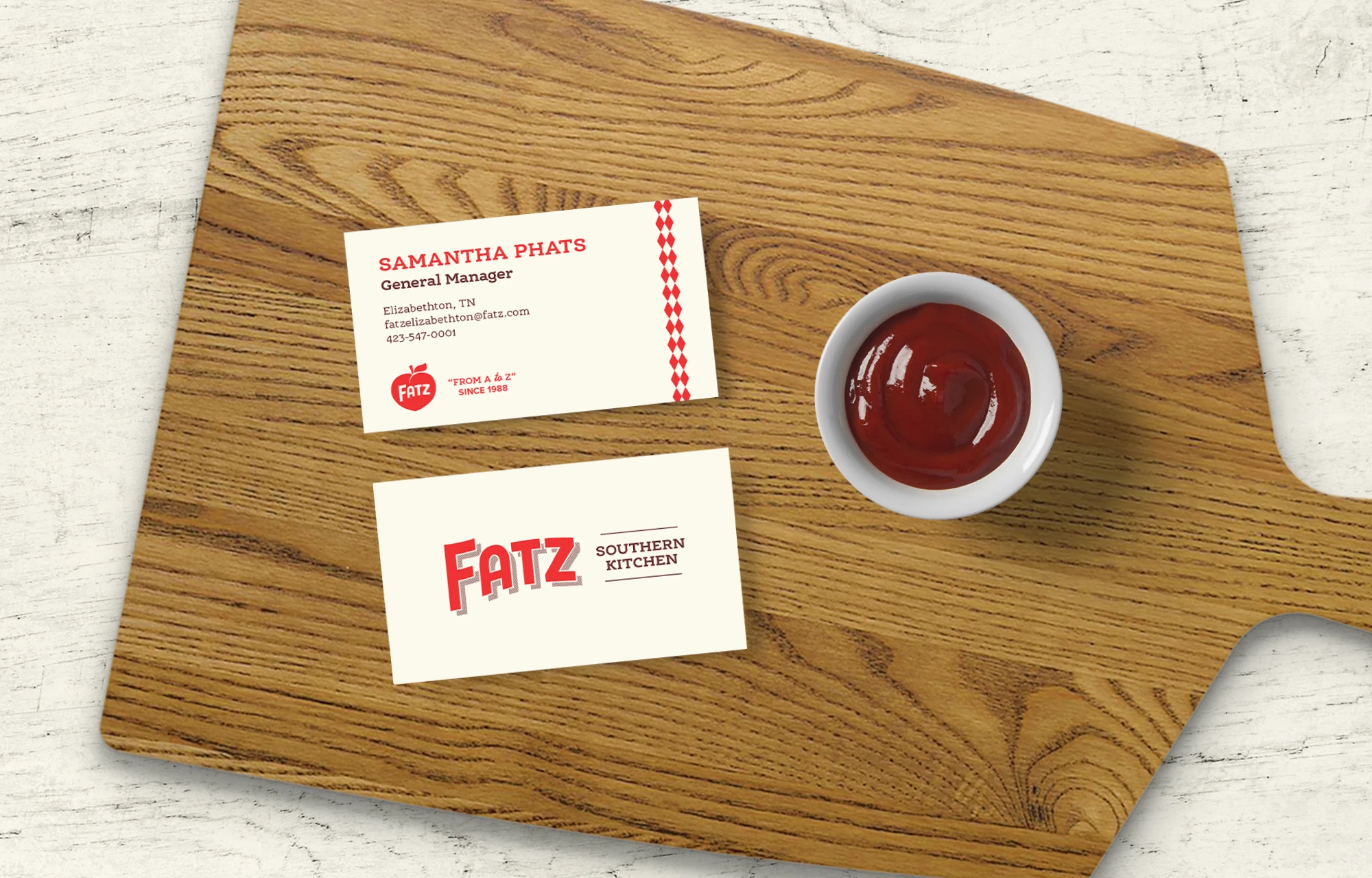 Front and back design of a business card, laid out on a cutting board with a ramekin of ketchup