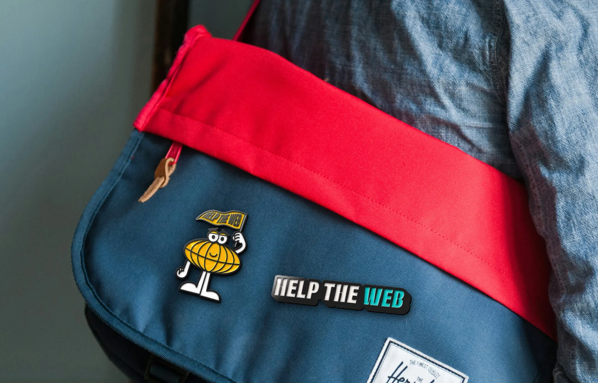 A Herschel laptop bag with two, Help the Web branded, enamel pins on it