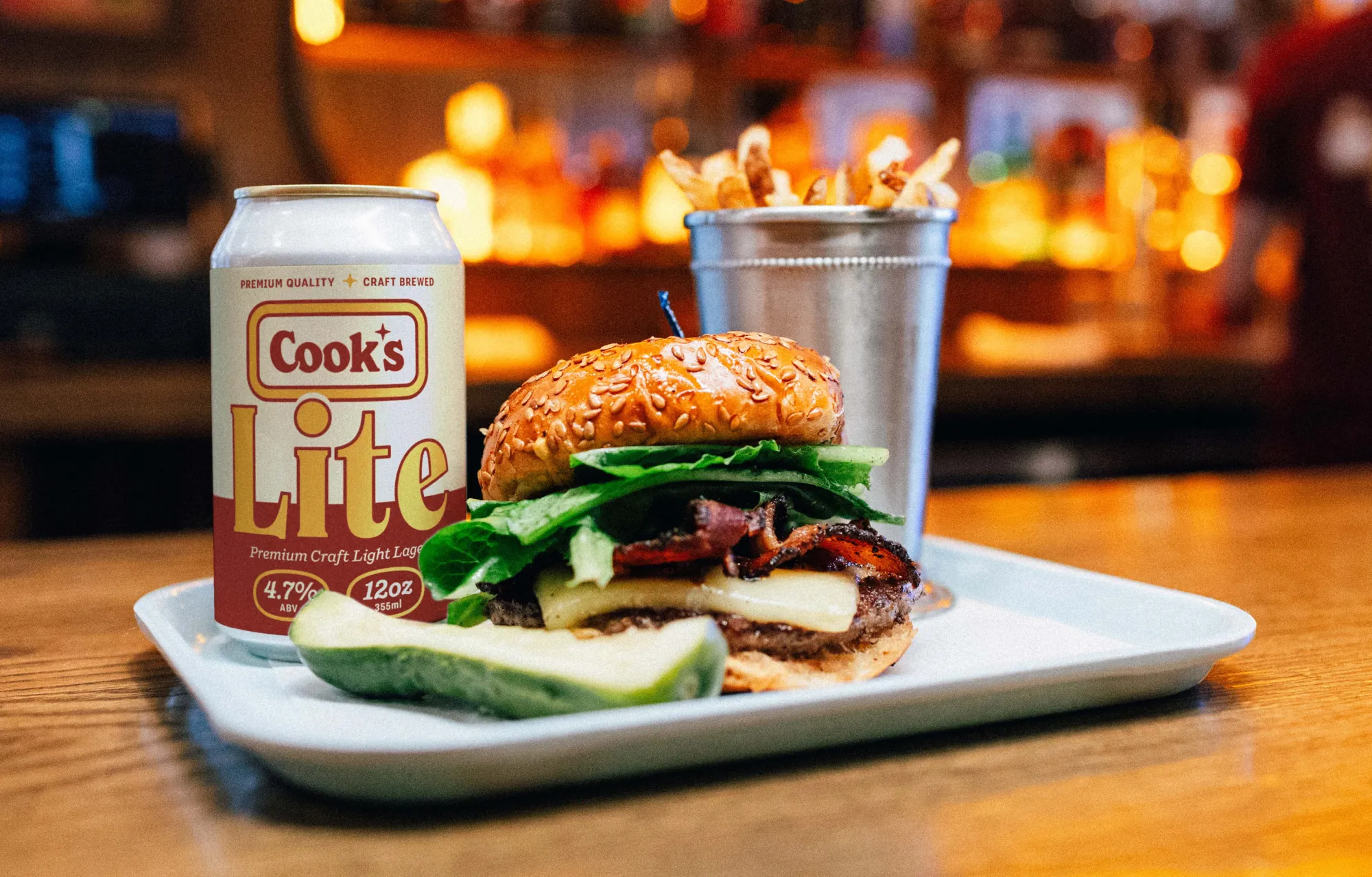 A beer can label, mocked up on a photo featuring a burger and fries at Cook's Burger Bar