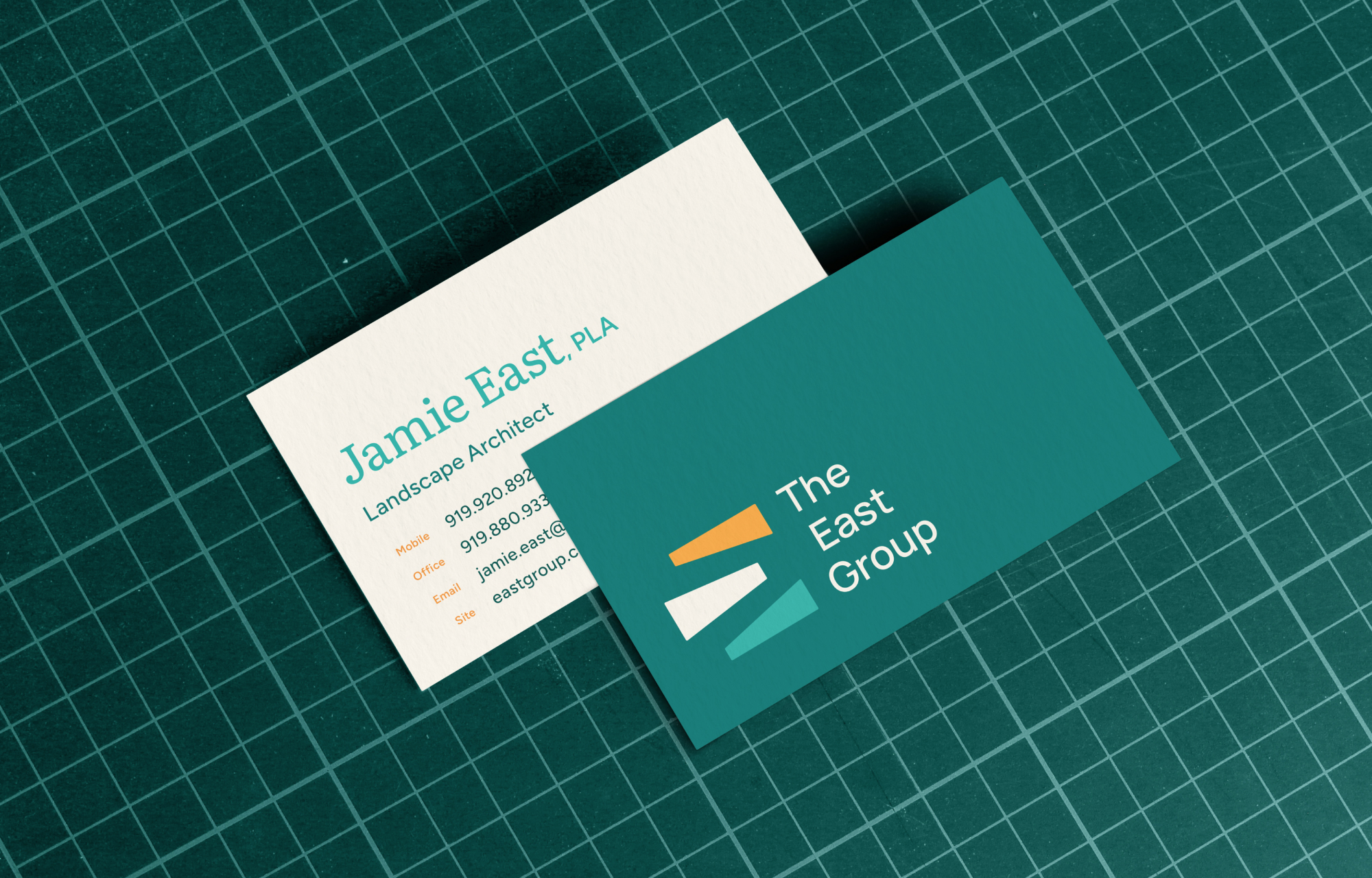 Front and back business card designs for The East Group, on a ruled cutting mat