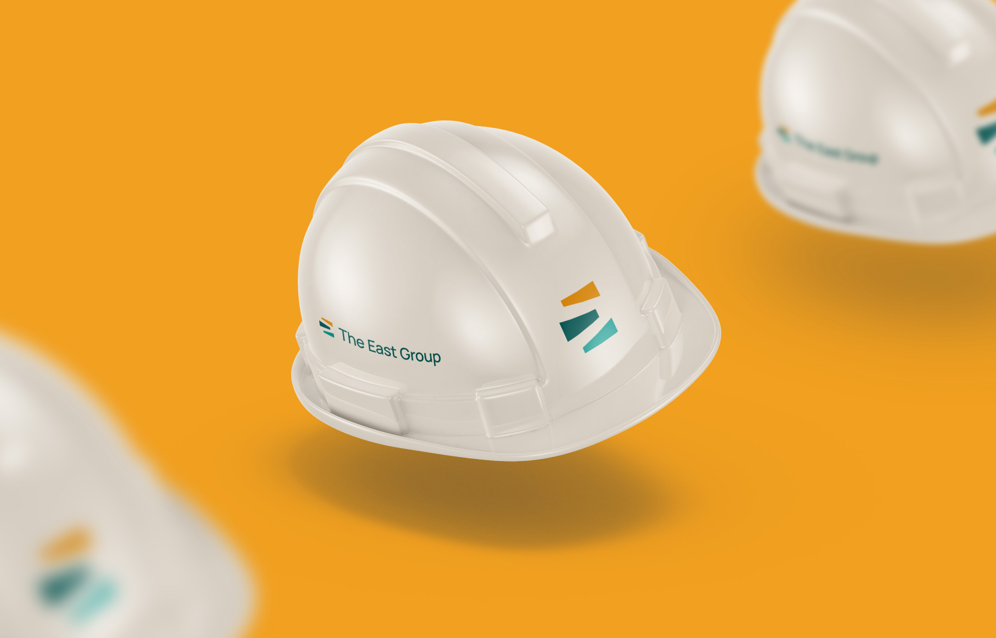 Floating hard hat mockup with The East Group logos, over an orange background