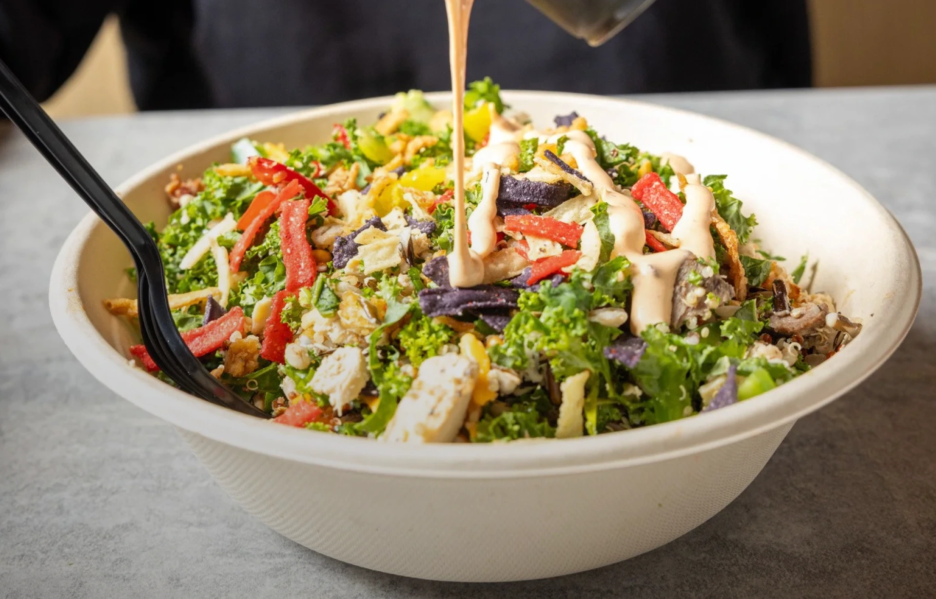 A fresh salad with dressing being poured onto it