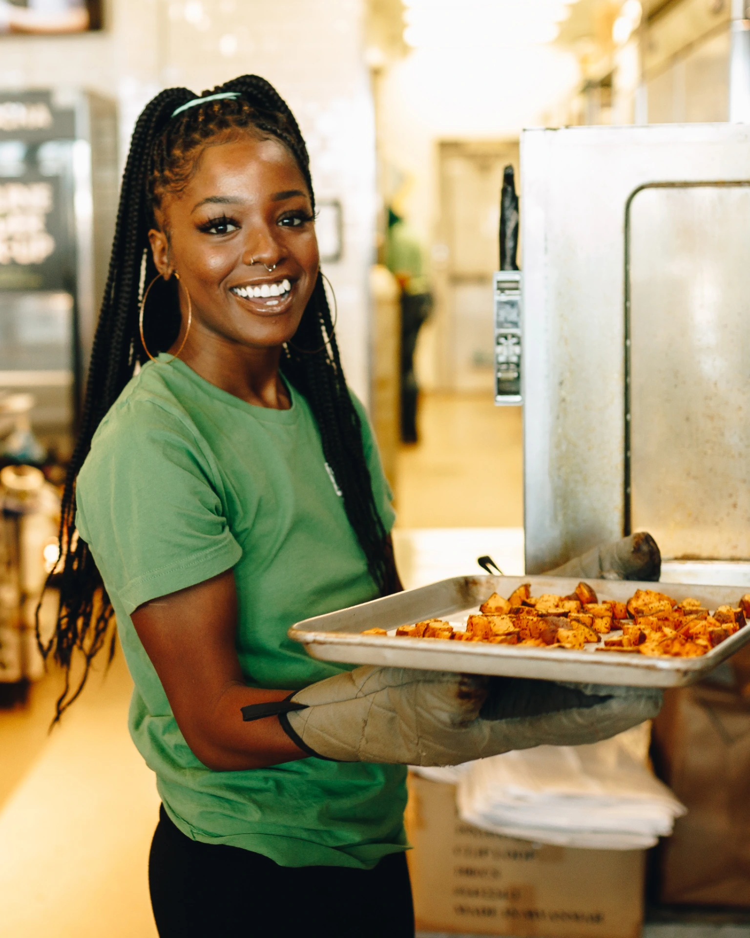 A smiling employee at DICED, putting a tray of ingredients in the oven to roast