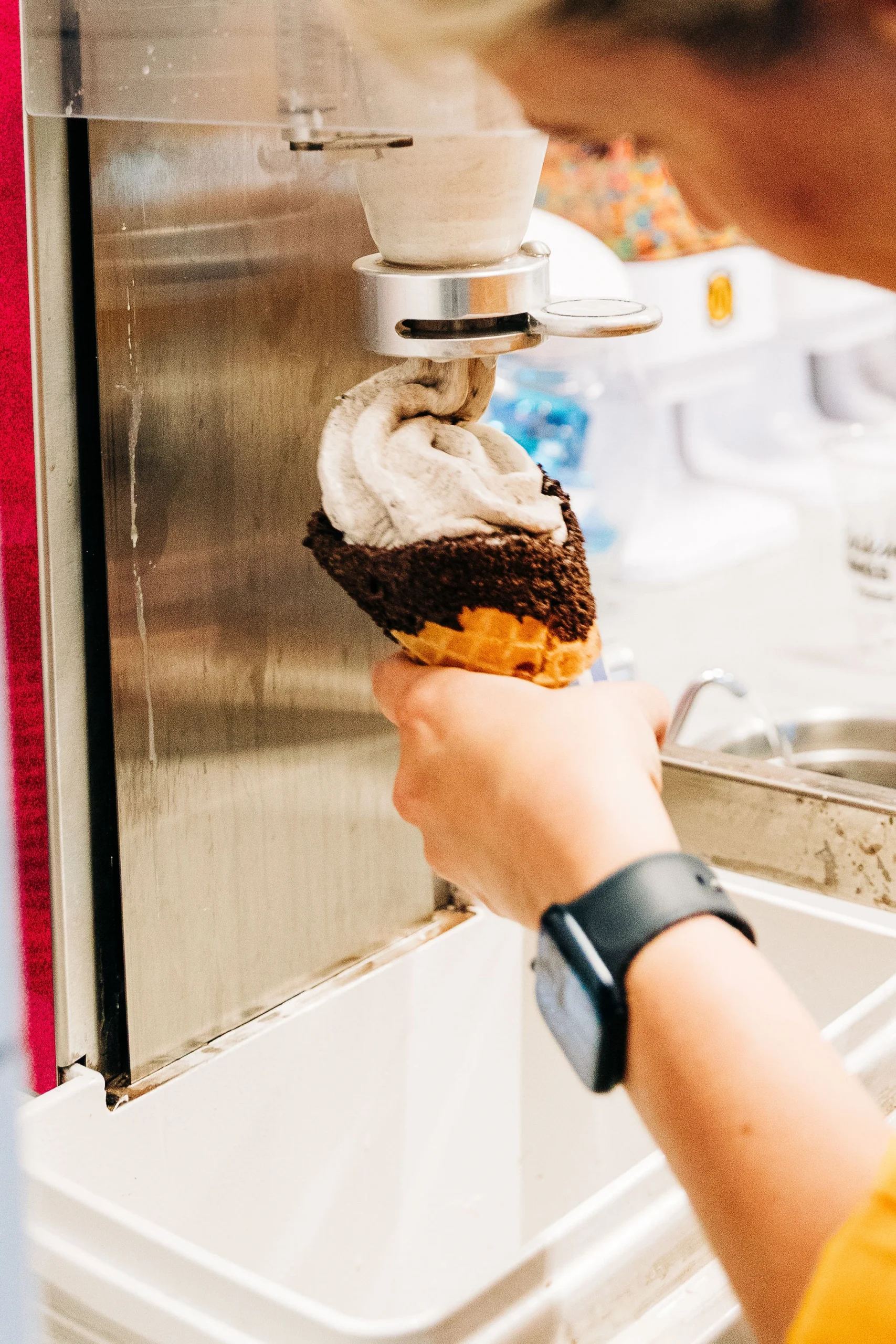 Filling a chocolate dipped waffle cone with soft serve at Mochichis Donut Shop