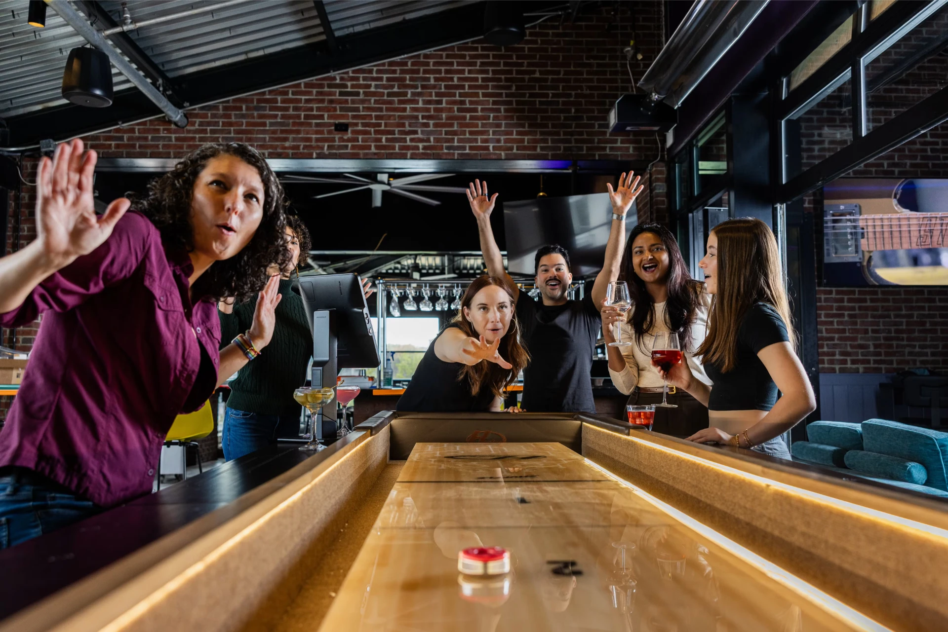 Friends cheer while playing shuffleboard at SMASH Social Club