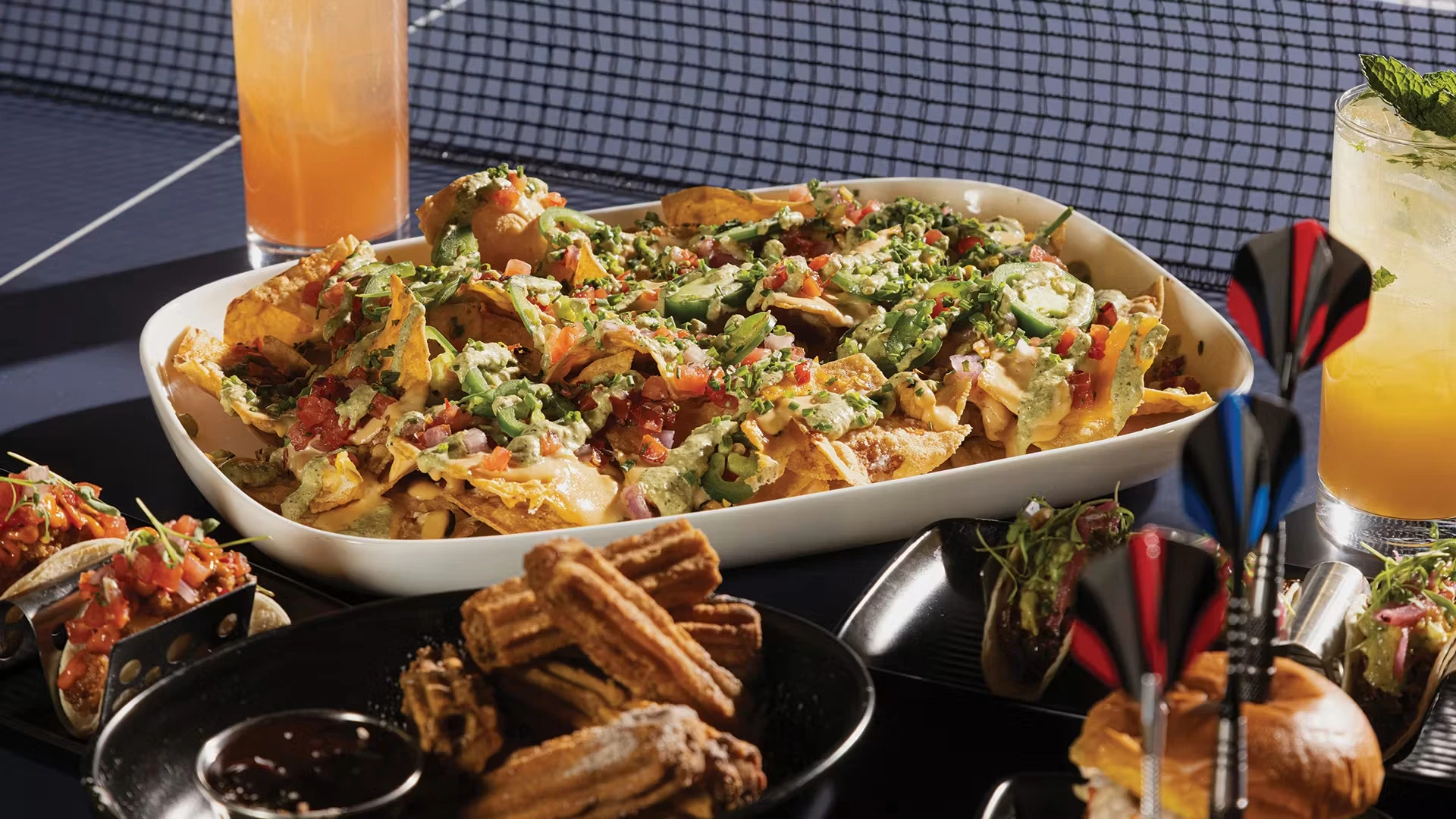 A plate of nachos amongst other food on a ping pong table at SMASH Social Club