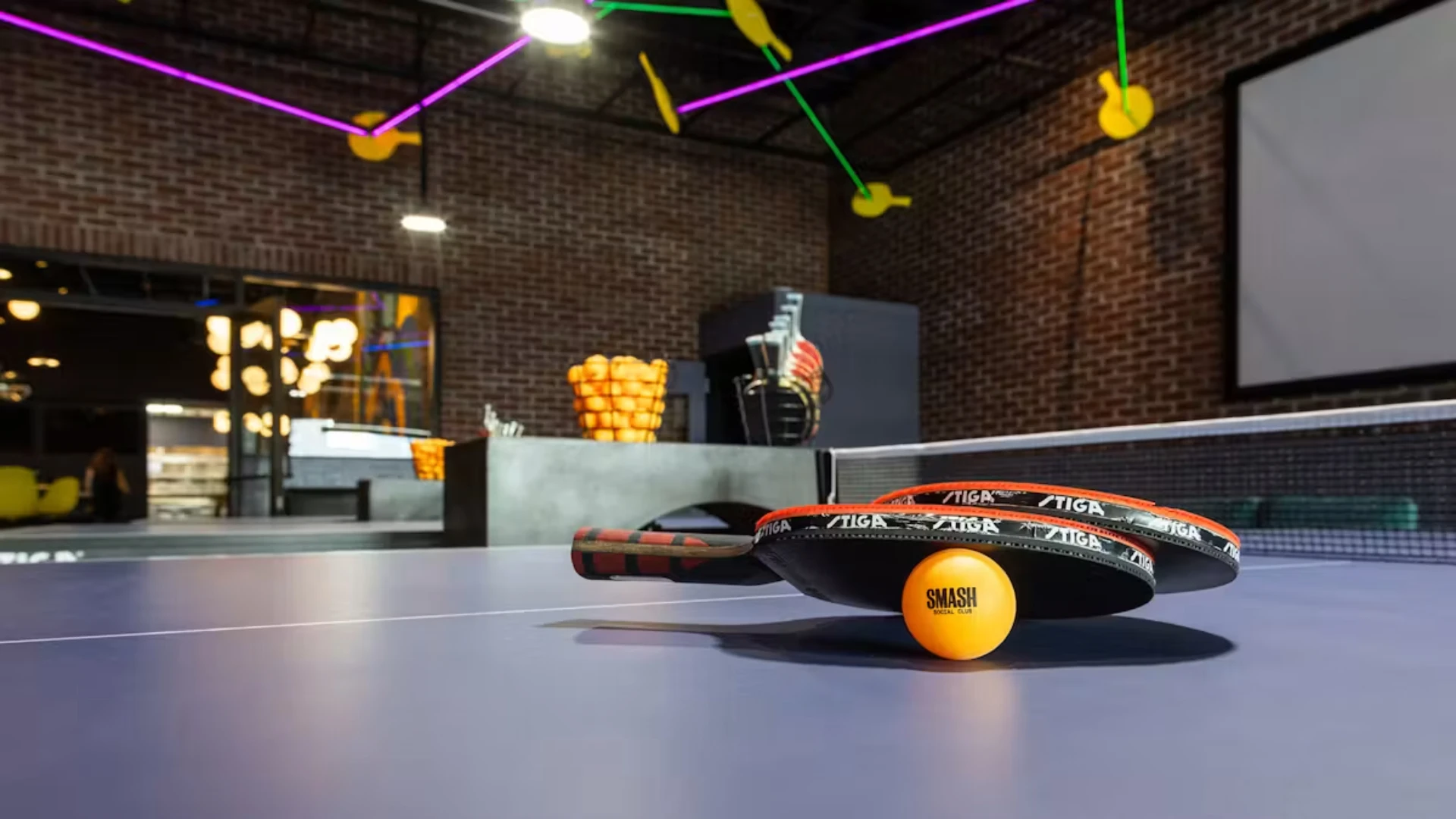Ping pong paddles sit on a table with a ping pong ball with the SMASH Social Club logo on it