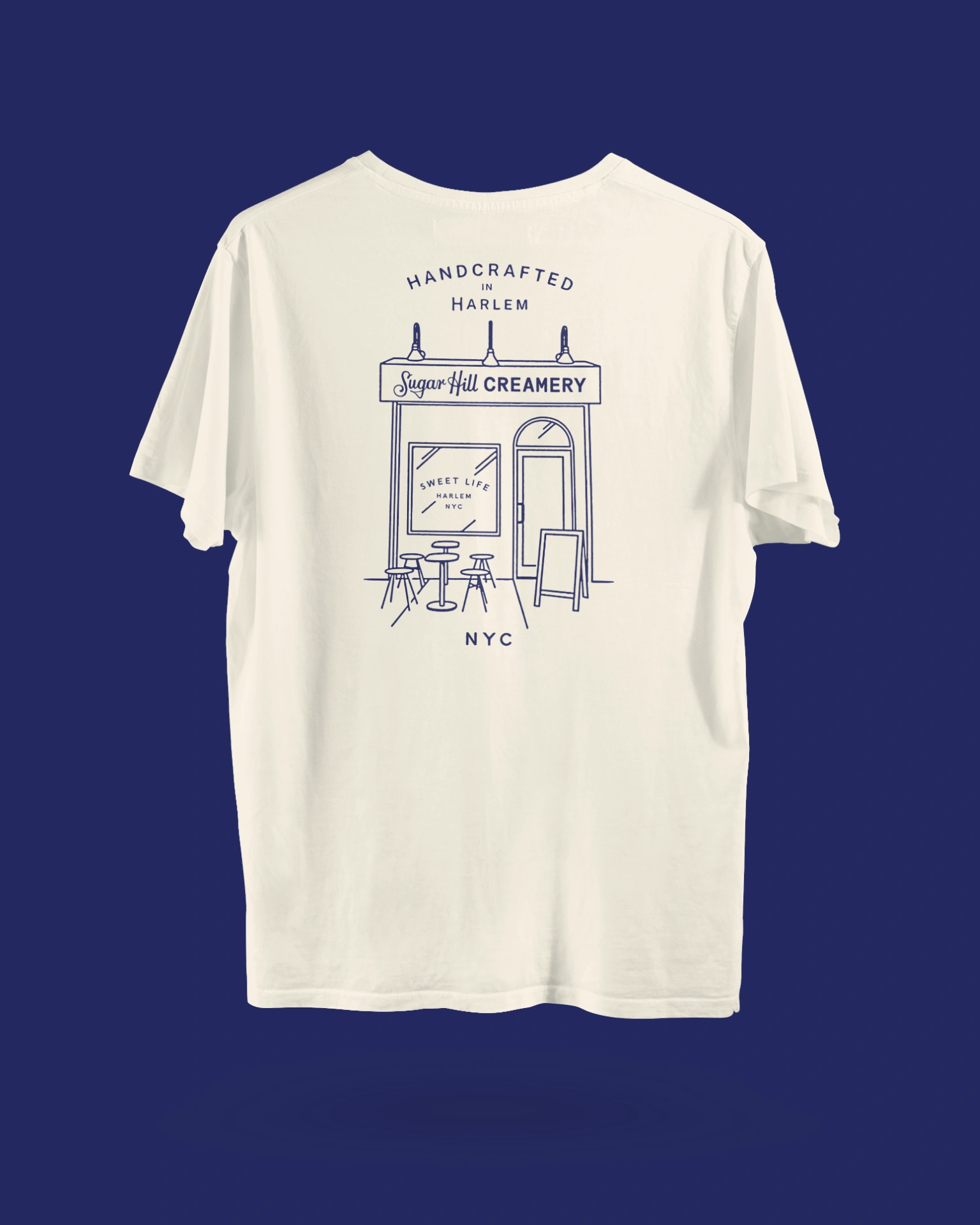 A white t-shirt with a back graphic of Sugar Hill Creamery's Harlem storefront location custom illustrated
