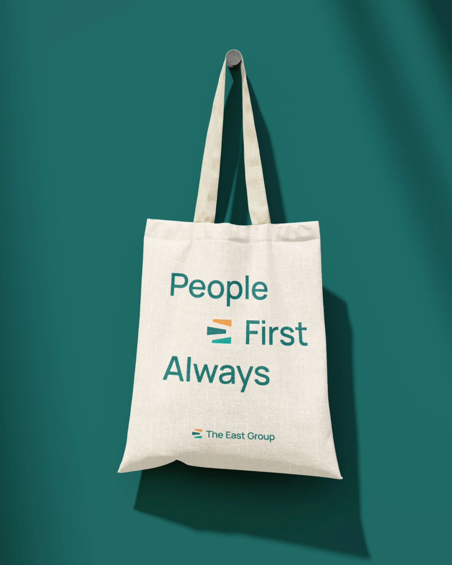 A tote bag with The East Group's tagline 'People First Always' hanging on a hook
