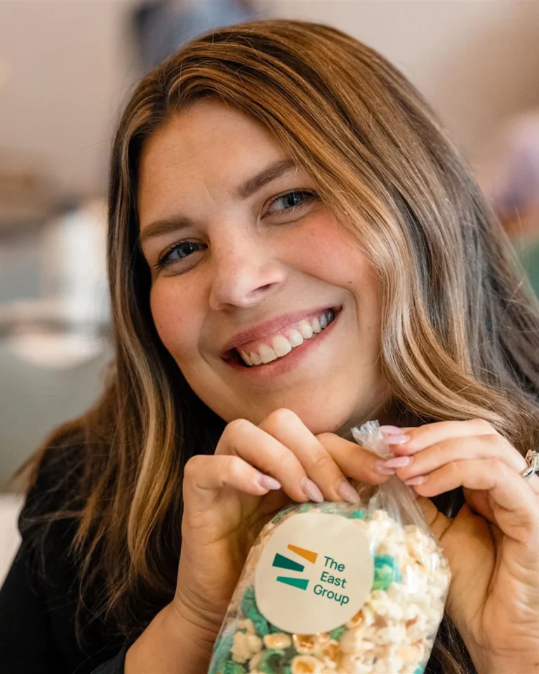 A smiling employee for The East Group holds up a bag of popcorn with a logo sticker on it