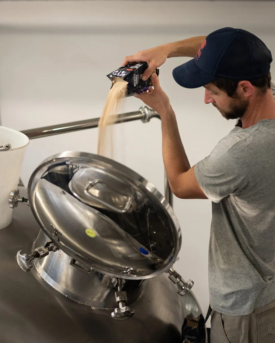 A man working at a brewery is pouring yeast into the fermentor