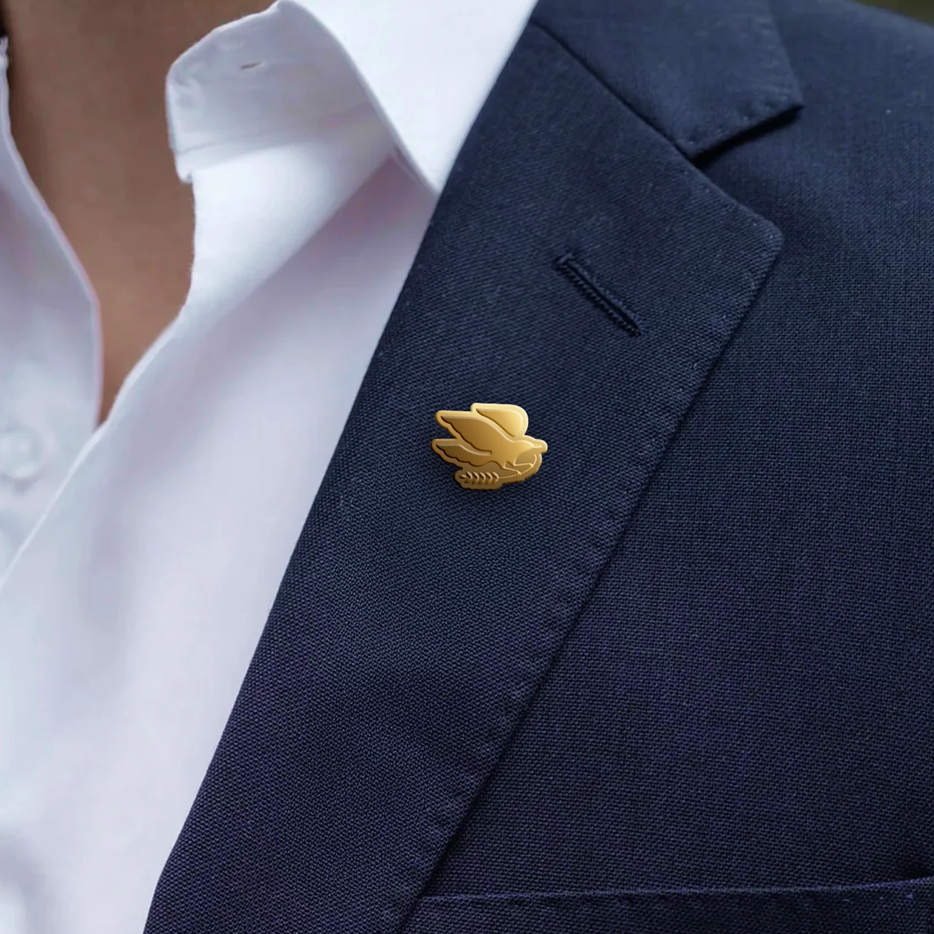 A gold enamel label pin of the Lee Segui mockingbird logo, pinned to a navy suit jacket